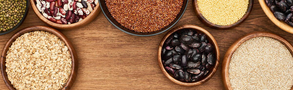 panoramic shot of bowls with oatmeal, buckwheat, beans and couscous on wooden surface