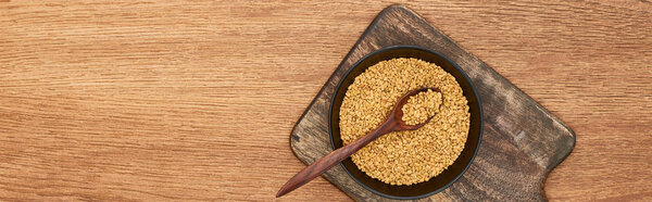panoramic shot of bowl with grains and spoon in it on wooden cutting board