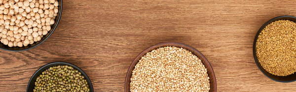 panoramic shot of bowls with chickpea, green beans and raw buckwheat on wooden surface
