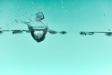 transparent ice cubes falling in water with splash on turquoise background clipart