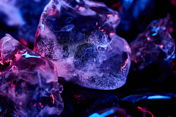 закрыть обзор прозрачных кубиков льда с фиолетовым освещением, изолированных на черном
