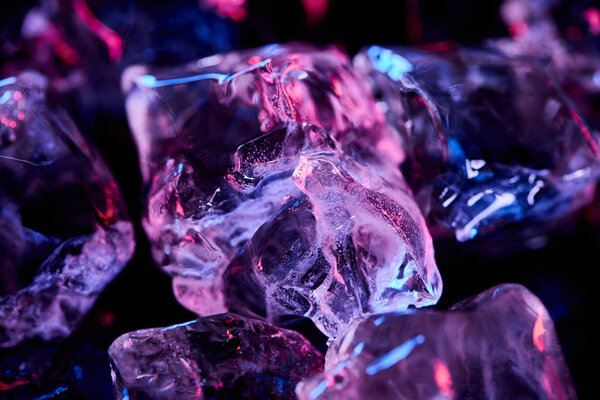 close up view of transparent ice cubes with purple lighting isolated on black