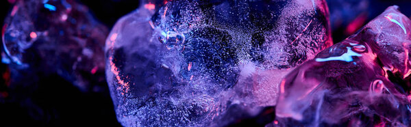 panoramic shot of transparent ice cubes with purple colorful lighting isolated on black
