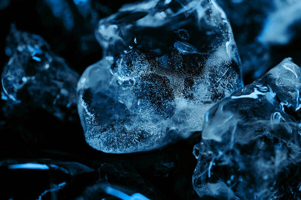 close up view of frozen ice cubes with blue lighting isolated on black