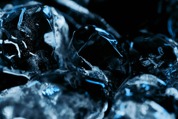 close up view of frozen ice cubes with blue lighting isolated on black