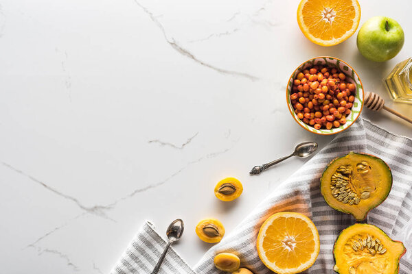 top view of striped towel with pumpkin, apricots, apple and orange near bowl with sea buckthorn on marble surface