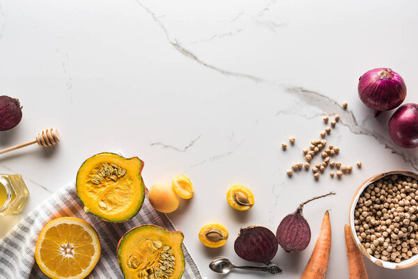 top view of textile with pumpkin, beetroot, onions, carrots and chickpea on marble surface