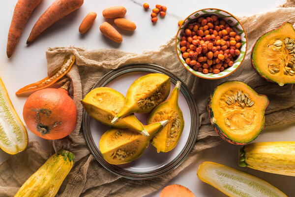 top view of plate with pumpkin on canvas near bowl with berries, carrots and zucchini