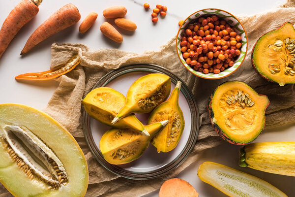 top view of plate with pumpkin on canvas near bowl with berries, carrots, melon and zucchini