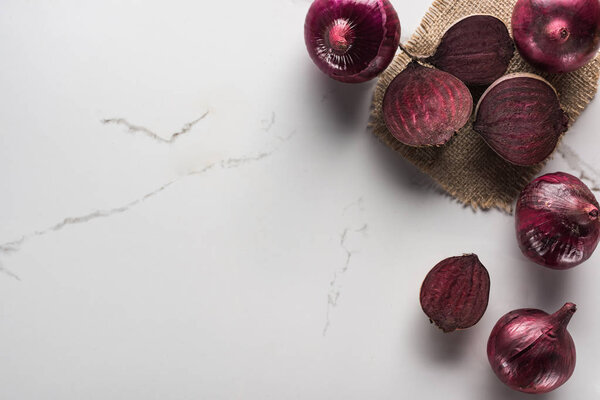 top view of red onions and beetroots on marble surface with hessian