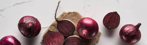 panoramic shot of red onions and beetroots on marble table with hessian