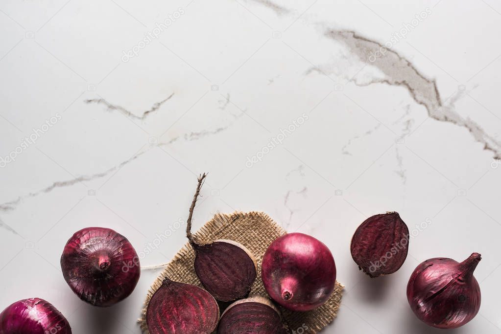 top view of beetroots and red onions on marble surface with hessian