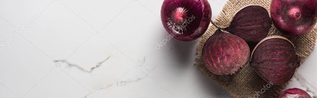 panoramic shot of beetroots and red onions on marble table with hessian
