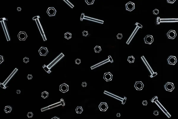 黒で分離された散乱金属ナットとボルトパターンの上図 — ストック写真