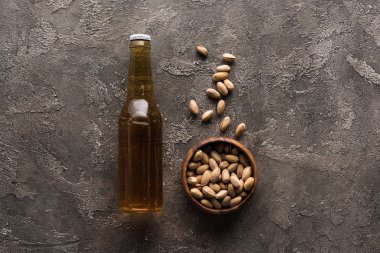 kahverengi yüzeyüzerinde hafif bira şişesi yakınında antep fıstığı ile kase üst görünümü