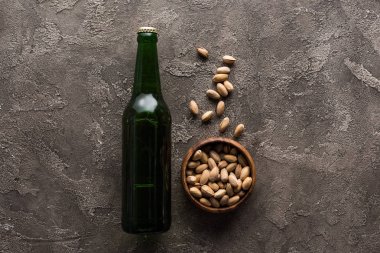 kahverengi yüzeyde bira yeşil şişe yakınında antep fıstığı ile kase üst görünümü