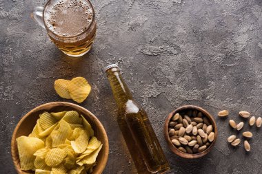 kahverengi yüzeyüzerinde şişe ve açık bira kupa yakın antep fıstığı ve cips ile kase üst görünümü