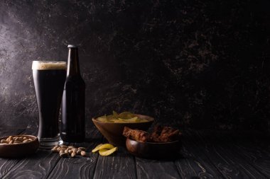 ahşap masada fındık, cips ve tavuk kanatları ile kase yakınında cam ve bira şişesi