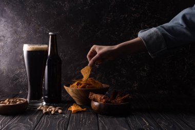 ahşap masada aperatifler ile şişe ve bira ve kase bardak yakın nachos parça alarak adam kırpılmış görünümü