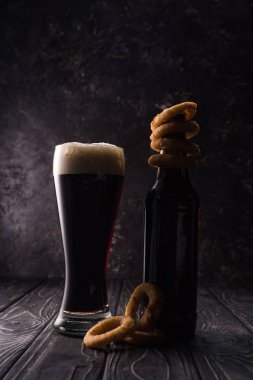 glass and bottle of beer with fried onion rings on wooden table clipart