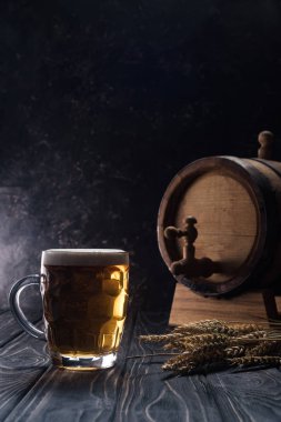 mug of light beer near small keg and wheat spikes on wooden table clipart