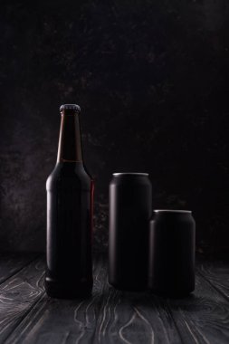 ahşap masa üzerinde bira şişe ve siyah metalik kutular 