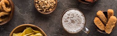 panoramic shot of mug of light beer near peanuts and crisps on brown textured surface clipart