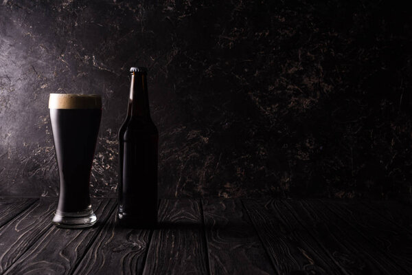 glass and bottle of dark beer on wooden table with shadow