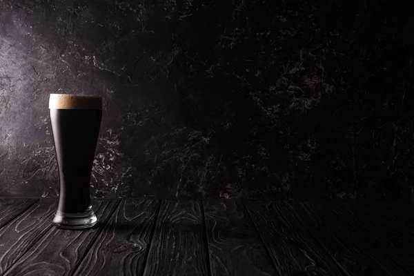 glass of dark beer on wooden table with shadow