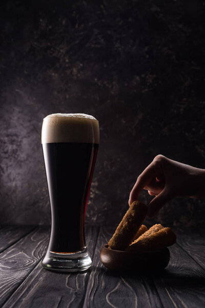 cropped view of man taking piece of fried cheese near glass of beer on wooden table