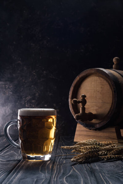 mug of light beer near small keg and wheat spikes on wooden table