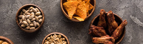 panoramic shot of bowls with nuts, nachos and roasted chicken wings