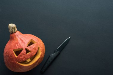 top view of spooky Halloween pumpkin with knife on black background clipart
