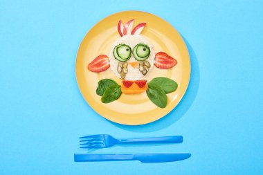 mavi arka plan üzerinde çatal yakın çocuk kahvaltı için gıda yapılmış fantezi yüz ile plaka üst görünümü