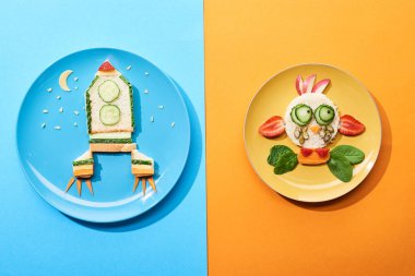 mavi ve turuncu arka plan üzerinde çocuk kahvaltı için gıda yapılmış fantezi yüz ve roket ile plakalar üst görünümü