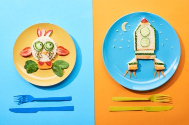 mavi ve turuncu arka plan üzerinde çatal yakın çocuklar için gıda yapılmış fantezi yüz ve roket ile plakalar üst görünümü