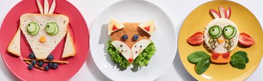 top view of plates with fancy cow, bird and fox made of food for childrens breakfast on white background, panoramic shot clipart