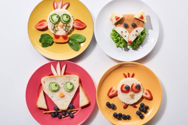 top view of plates with fancy animals made of food for childrens breakfast on white background clipart