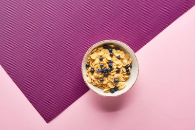 top view of bowl with breakfast cereal and blueberry on purple and pink background clipart
