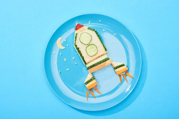 top view of plate with rocket made of food for childrens breakfast on blue background