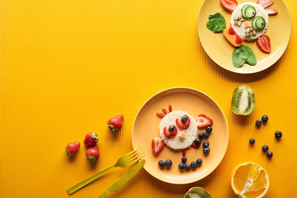 カラフルなオレンジ色の背景にカトラリーの近くの食品で作られた派手な動物とプレートのトップビュー — ストック写真