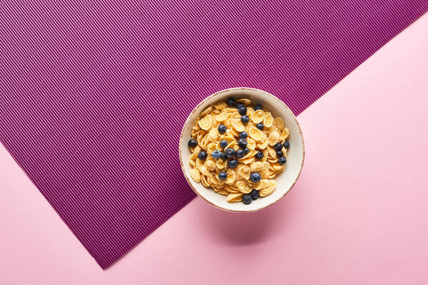 top view of bowl with breakfast cereal and blueberry on purple and pink background