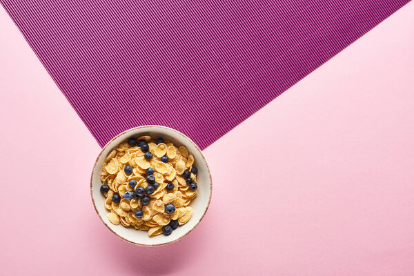 top view of bowl with breakfast cereal and blueberry on purple and pink background