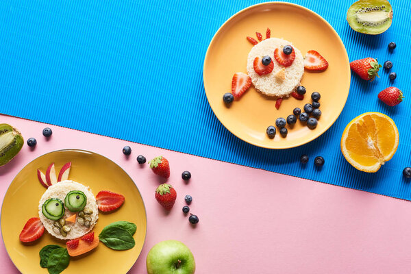 top view of plates with fancy animals made of food on blue and pink background