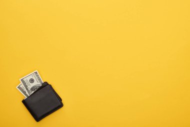 Sarı arka planda dolar banknotları olan cüzdanın üst görüntüsü