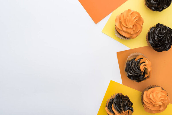 вид на вкусные кексы Хэллоуин на желтом, оранжевом и белом фоне с копировальным пространством
