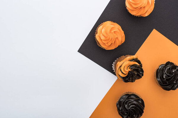 вид на вкусные кексы Хэллоуин на черном, оранжевом и белом фоне с копировальным пространством
