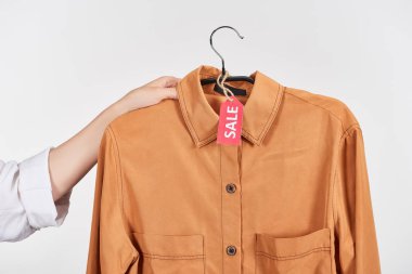 cropped view of woman holding hanger with shirt with sale label isolated on white clipart