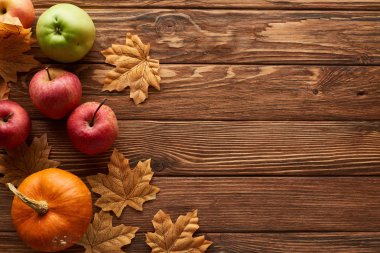 top view of small pumpkin and apples on brown wooden surface with dried autumn leaves clipart