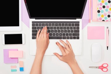 menekşe ve beyaz arka plan üzerinde gadget'lar ve ofis malzemeleri yakınında dizüstü bilgisayar kullanarak kadın kısmi görünümü